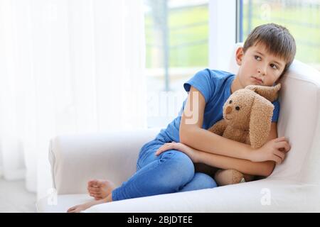 Triste ragazzino seduto in poltrona a casa Foto Stock