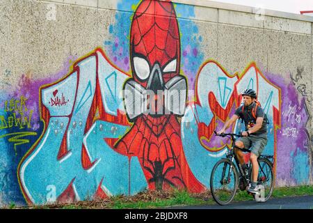 Hamm/Germania, 29 aprile 2020: Poeple che passa un graffiti coronavirus dell'artista di strada „Uzey" che mostra Spiderman con una maschera di protezione su un muro a Hamm, Germania --- Hamm, 29.4.2020 - Corona-Kunst. Das Graffiti SPIDERMAN mit Atemmaske hat der Graffiti-Künstler Kai „Uzey Wohlgemuth an eine Wand in Hamm gesprüht. Foto Stock