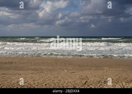 Onde del mare con schiuma bianca, durante una giornata ventosa e piovosa in autunno. Linea di spiaggia di sabbia. Nuvole colorate e intense. Rethymnon, Creta, Grecia. Foto Stock