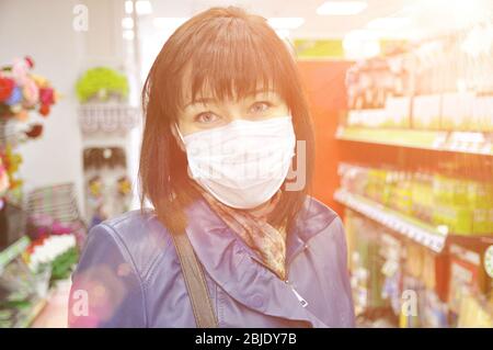 Giovane donna europea in giacca di pelle blu e maschera contro le infezioni in negozio. Protezione e prevenzione delle misure durante un'epidemia. Svasatura Foto Stock