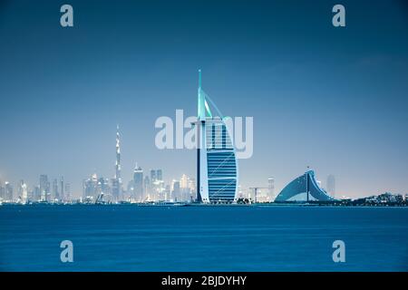 Ammira il paesaggio urbano di Dubai attraverso il mare dopo il tramonto. Dubai, Emirati Arabi Uniti. Foto Stock