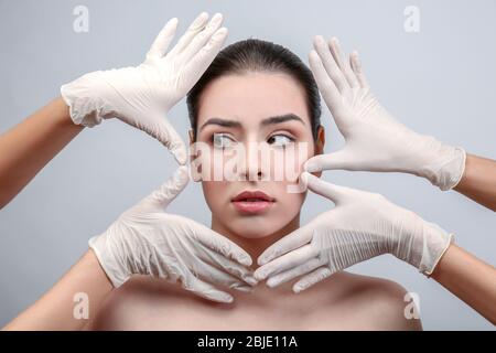 Mani in guanti di gomma che toccano il viso di giovane bella donna, su sfondo chiaro Foto Stock