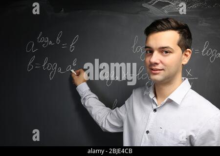 Bel giovane insegnante scrivere formule matematiche sulla lavagna Foto Stock
