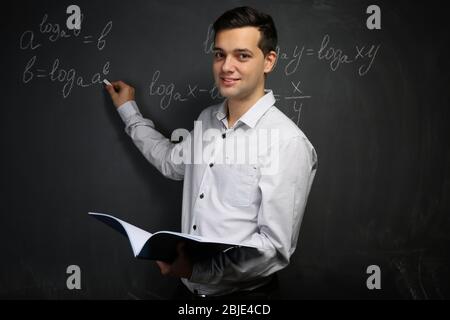 Bel giovane insegnante scrivere formule matematiche sulla lavagna Foto Stock