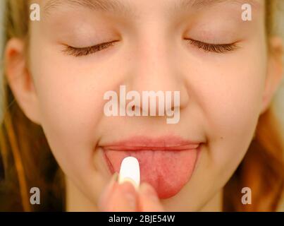 Faccia di una ragazza bionda mette una pillola sulla sua lingua, prendendo la medicina dal mal di testa, dal dolore dello stomaco o prendendo le vitamine, meds di sedazione, concetto di sanità Foto Stock