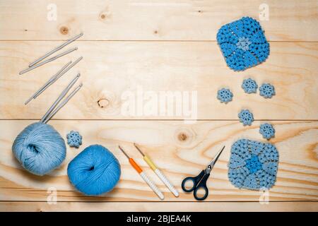 Accessori e utensili per maglieria, filato colorato, tovaglioli a motivi quadrati con crochet blu, ganci, forbici su fondo in legno chiaro vista dall'alto Foto Stock