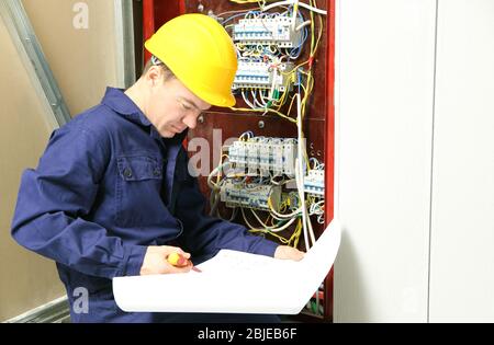 Elettricista che controlla i collegamenti nella scheda di distribuzione secondo lo schema elettrico Foto Stock