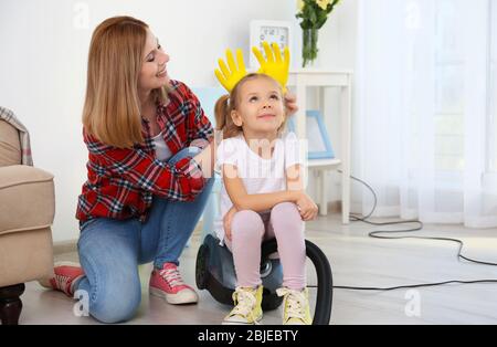 Bambina e sua madre giocando mentre fa pulizia a casa Foto Stock