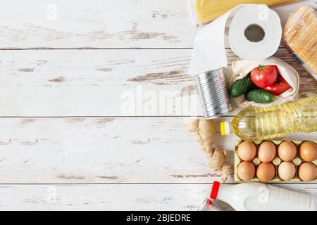 Vari prodotti alimentari come pasta, uova, cibo in scatola, bottiglia di latte e olio vista dall'alto su sfondo di legno. Donazione di cibo, servizio di consegna sicuro con Foto Stock