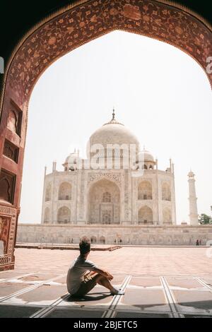 Il giovane uomo siede sotto il cancello e guarda il Taj Mahal ad Agra Foto Stock