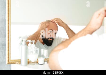 Uomo adulto con problemi di perdita dei capelli guardando nello specchio a casa Foto Stock