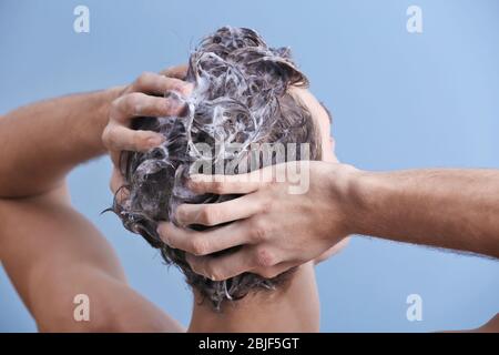 Giovane uomo che lava i capelli su sfondo colore Foto Stock