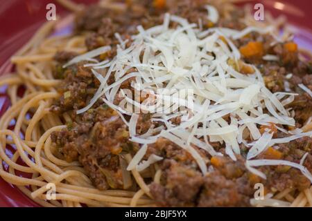 Da vicino si può ammirare un tradizionale piatto fatto in casa agli Spaghetti Bolognese in un piatto rosso con parmigiano Foto Stock