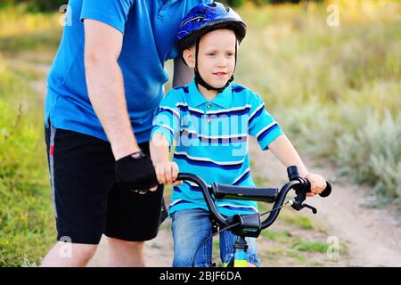 padre insegna un bambino di un figlio in un casco protettivo a guidare una bicicletta. Foto Stock