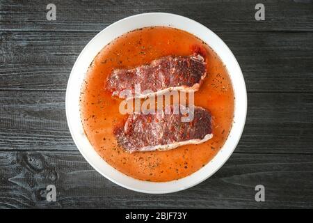 Ciotola con bistecche in marinata a tavola Foto Stock