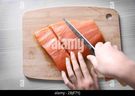 Mani femminili con coltello che tagliano il filetto di salmone fresco su tavola di legno Foto Stock