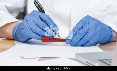 Mano di un medico che tiene un flaconcino di campione di sangue e scrive a lime, Closeup Foto Stock