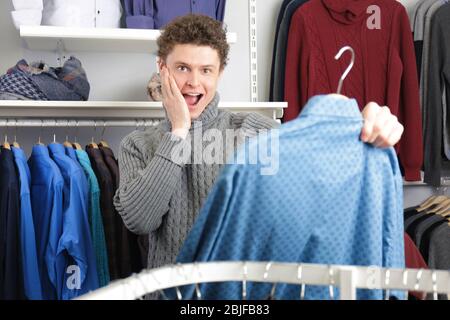 Bel giovane uomo che sceglie vestiti in negozio moderno Foto Stock