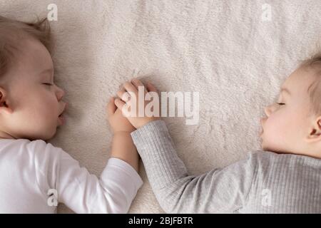 Infanzia, sonno, relax, famiglia, stile di vita concetto - due bambini 2 e 3 anni vestiti con tuta bianca e beige dormire su un beige Foto Stock
