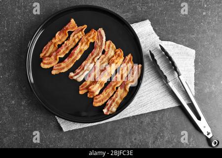 Gustose fette di pancetta con tenaglie sul tavolo Foto Stock