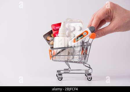 Cliente che acquista enorme quantità di pillole concetto. Ritagliato foto ravvicinata di mano spingendo carrello pieno di diverse droghe isolato sfondo grigio wi Foto Stock