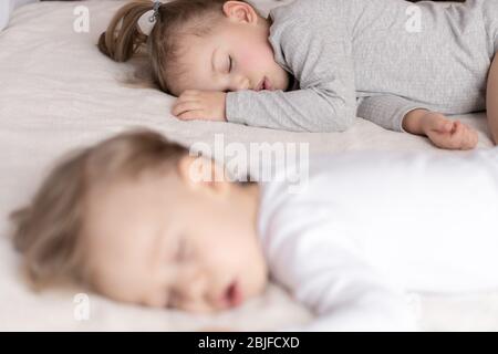 Infanzia, sonno, relax, famiglia, stile di vita concetto - due bambini 2 e 3 anni vestiti con tuta bianca e beige dormire su un beige Foto Stock