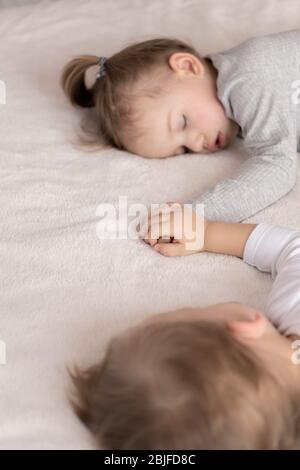 Infanzia, sonno, relax, famiglia, stile di vita concetto - due bambini 2 e 3 anni vestiti con tuta bianca e beige dormire su un beige Foto Stock