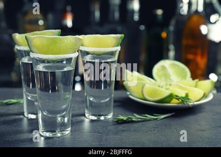 Tequila con succose fette di lime e sale su sfondo sfocato di bottiglie di vetro Foto Stock