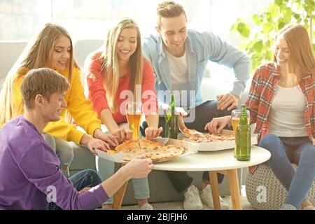 Amici con gustosa pizza e birra a casa festa Foto Stock