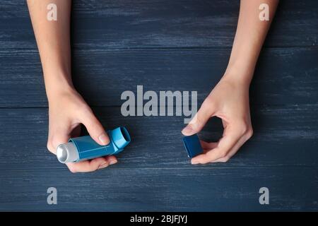 Mani femminili che tengono l'inalatore di asma su sfondo di legno Foto Stock