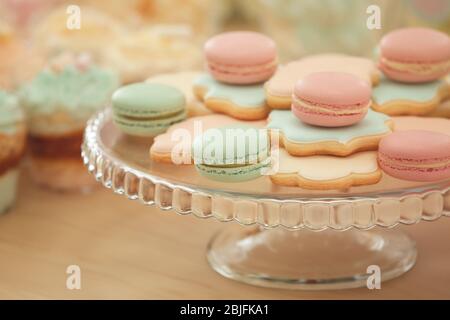 Stativo in vetro con gustosi macaron e biscotti sul tavolo, primo piano Foto Stock