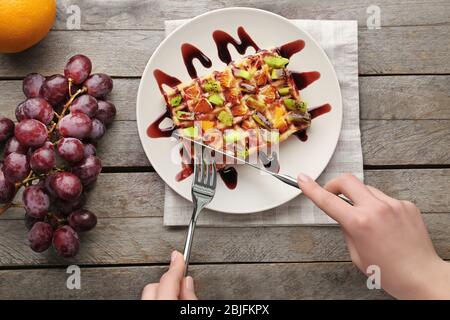 Donna che mangia deliziosi waffle con frutta e sciroppo su piatto bianco Foto Stock