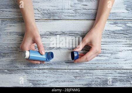 Mani femminili che tengono l'inalatore di asma su sfondo di legno Foto Stock