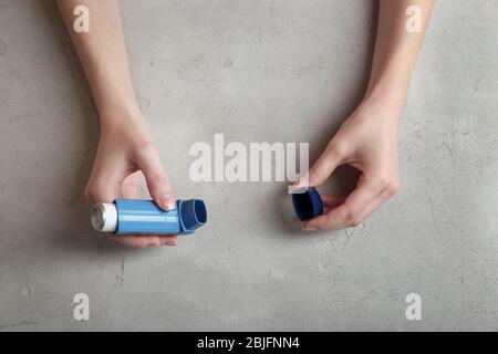 Mani femminili che tengono l'inalatore per asma su sfondo grigio strutturato Foto Stock