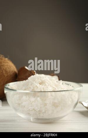 Ciotola di vetro con scaglie di cocco su tavolo di legno Foto Stock