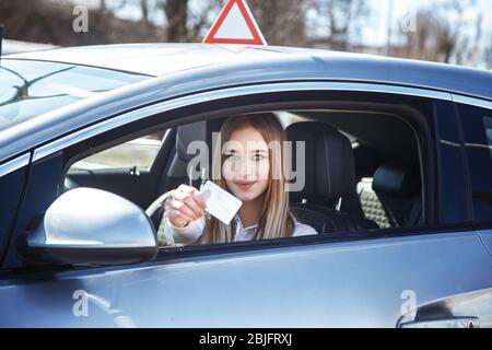 Ragazza gioiosa che guida un'auto da addestramento con una carta di patente di guida nelle sue mani Foto Stock