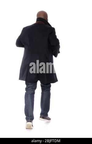 Figura maschile a corpo pieno torna alla vista della fotocamera di un uomo afro-americano che indossa un trench blu marino con jeans blu denim e scarpe marrone casual Foto Stock
