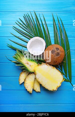 Delizioso ananas a fette e cocco fresco con foglia di palma su sfondo di legno blu Foto Stock