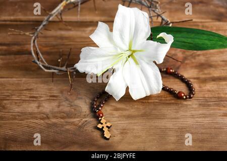 Composizione con rosario, giglio e corona di spine su sfondo ligneo Foto Stock