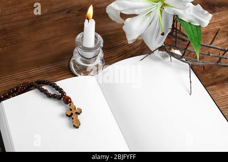 Libro bianco aperto, candela con supporto, rosario e corona di spine su tavola di legno Foto Stock