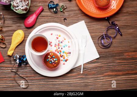 Piatto con cupcake di compleanno e vetro di carta su tavolo di legno Foto Stock