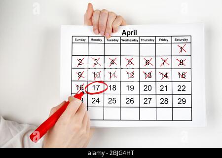 Donna che segna la data in calendario su sfondo bianco muro Foto Stock