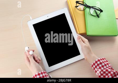 Donna che tiene gli auricolari e il tablet sul tavolo. Concetto di audiolibro Foto Stock