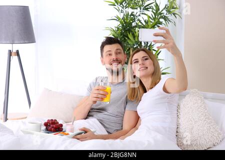 Coppia che ha la colazione a letto e prendere selfie Foto Stock