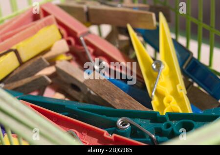 I clothespins di plastica multicolore mescolati insieme con altri clothespins di legno in un cestino verde Foto Stock