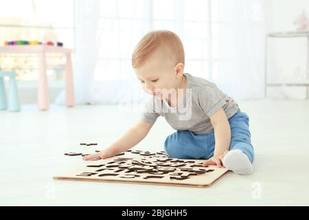 Bambino carino che gioca con le lettere mentre siede sul pavimento a casa Foto Stock