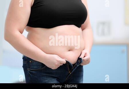 Stout donna adulta cercando di mettere sul jeans stretti a casa. La perdita di peso concept Foto Stock