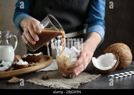 Donna che versa caffè freddo di cocco in vetro con cubetti di ghiaccio sul tavolo Foto Stock