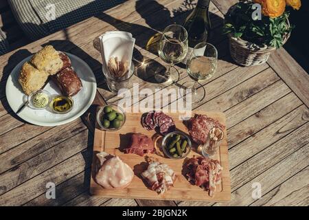 Salumi serviti con vino bianco all'aperto. Un piatto di prosciutto e pancetta affettare con sottaceti su una tavola di legno Foto Stock