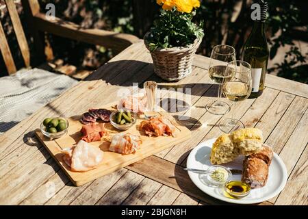 Salumi serviti con vino bianco all'aperto. Un piatto di prosciutto e pancetta affettare con sottaceti su una tavola di legno Foto Stock